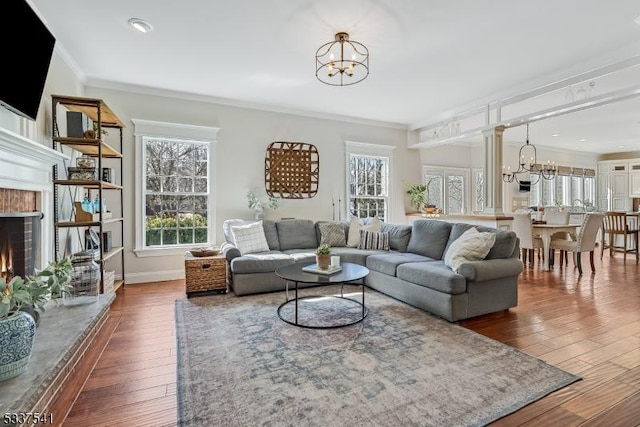 living room featuring baseboards, dark wood finished floors, ornamental molding, a fireplace, and a chandelier