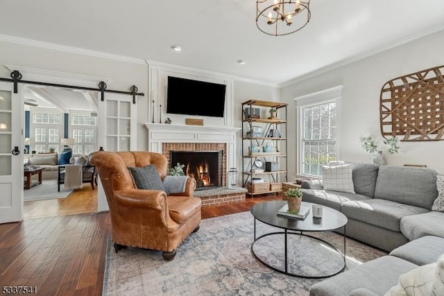 living room with a barn door, a fireplace, ornamental molding, and wood finished floors