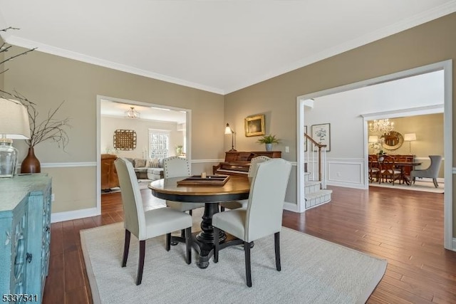 dining space featuring ornamental molding, wood finished floors, stairway, and an inviting chandelier