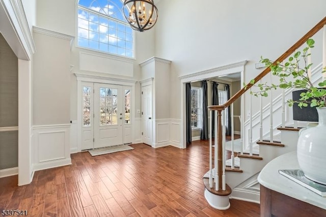 foyer featuring a wainscoted wall, stairway, wood finished floors, and an inviting chandelier