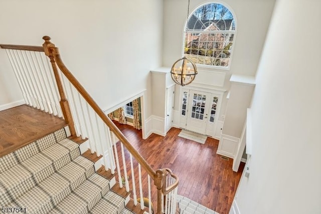 stairs featuring a chandelier, a towering ceiling, baseboards, and wood finished floors