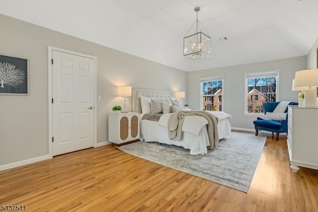 bedroom with a chandelier, light wood-type flooring, vaulted ceiling, and baseboards