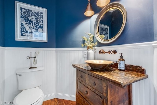 half bathroom with a wainscoted wall, vanity, toilet, and wood finished floors