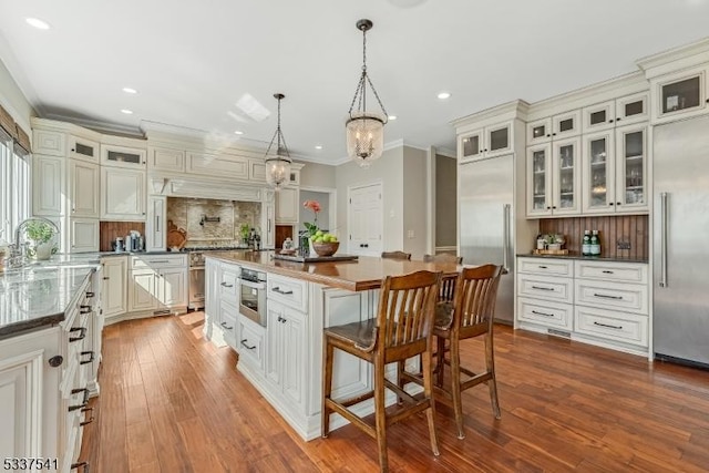 kitchen featuring dark countertops, hanging light fixtures, glass insert cabinets, a kitchen island, and built in refrigerator