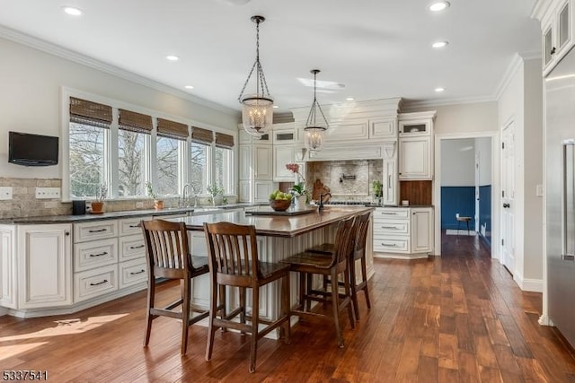 kitchen with decorative light fixtures, dark countertops, glass insert cabinets, ornamental molding, and a kitchen island