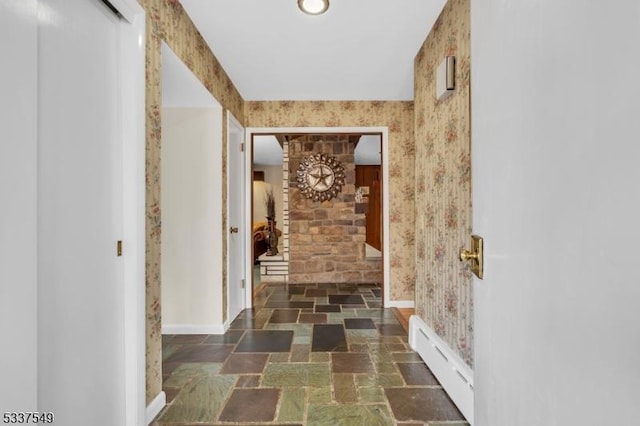 hall featuring stone tile flooring, baseboards, baseboard heating, and wallpapered walls