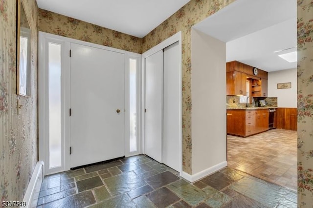 entrance foyer with baseboards, plenty of natural light, stone tile flooring, and wallpapered walls