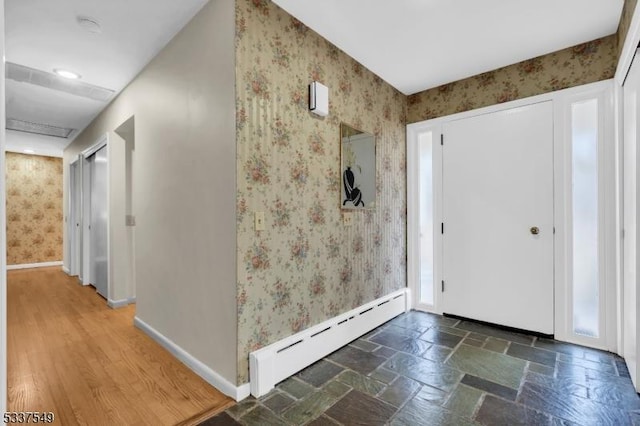 foyer entrance with wallpapered walls, baseboards, a baseboard heating unit, and stone tile floors