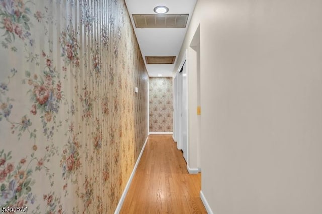 hallway with light wood-style floors, visible vents, baseboards, and wallpapered walls