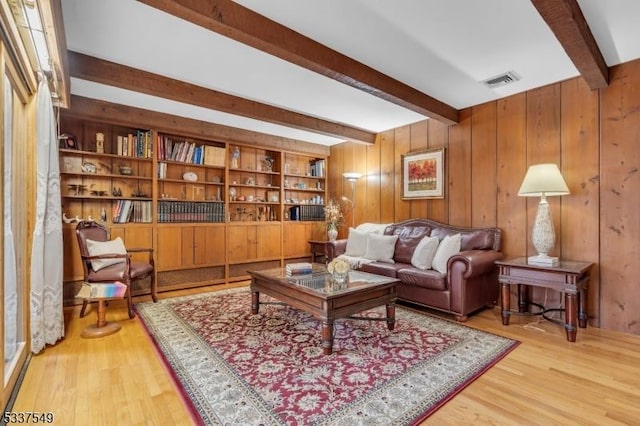 living area featuring wood walls, visible vents, wood finished floors, and beamed ceiling