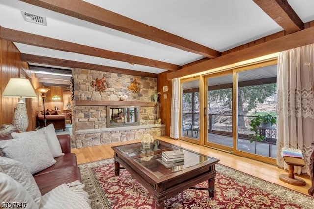 living area with beam ceiling, a fireplace, visible vents, wood walls, and wood finished floors