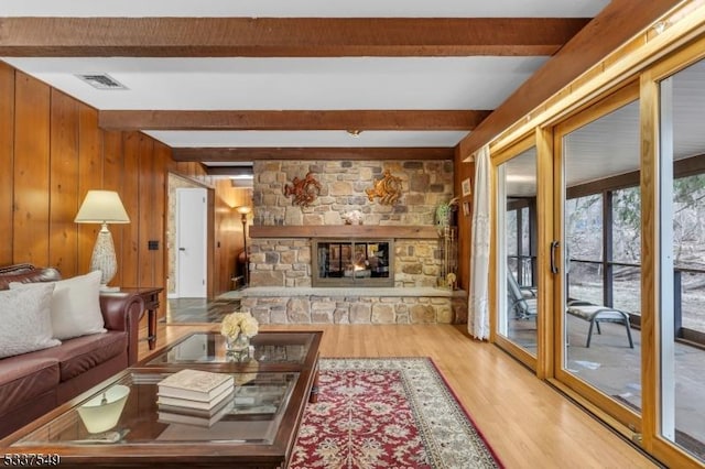 living area with visible vents, beamed ceiling, wood finished floors, a stone fireplace, and wood walls