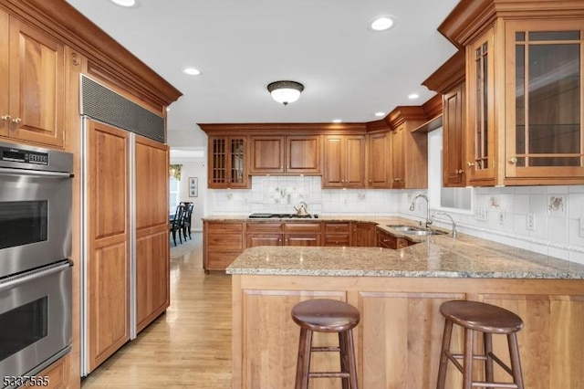 kitchen featuring a breakfast bar area, glass insert cabinets, light stone counters, double oven, and a sink