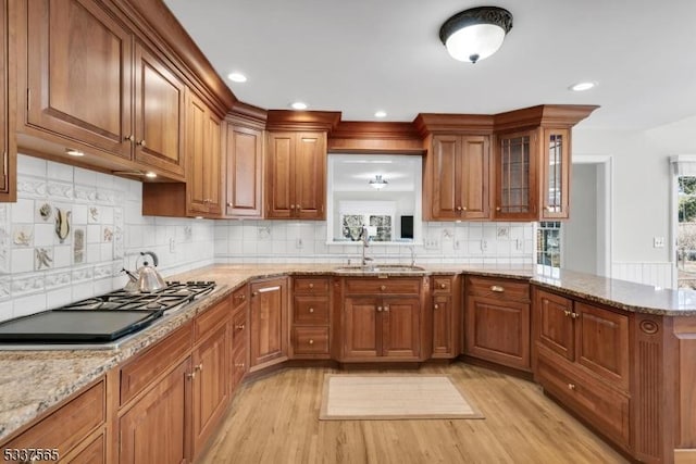 kitchen with brown cabinets, glass insert cabinets, a sink, black gas stovetop, and a peninsula