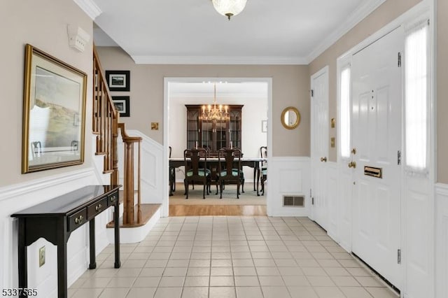 entryway featuring a chandelier, ornamental molding, wainscoting, and visible vents