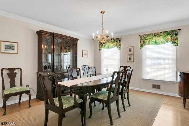 dining room featuring a chandelier, visible vents, baseboards, light wood-style floors, and ornamental molding