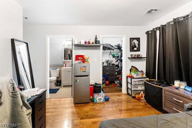 bedroom featuring a spacious closet, stainless steel fridge, a closet, and light wood-type flooring