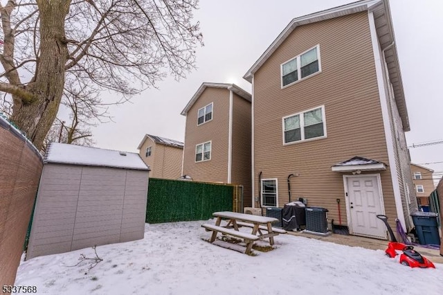 snow covered house with central AC unit and a shed