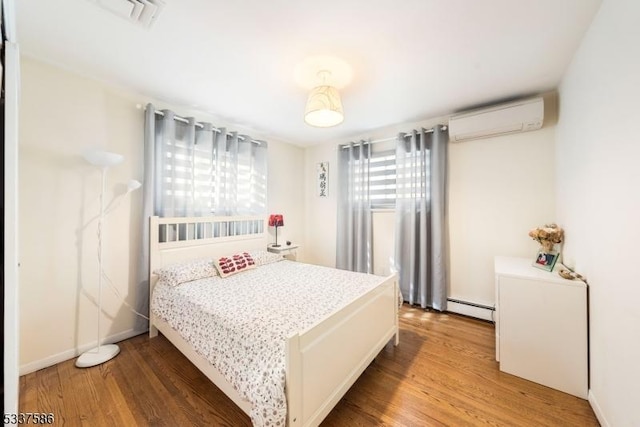 bedroom with wood-type flooring, a baseboard heating unit, and a wall mounted air conditioner