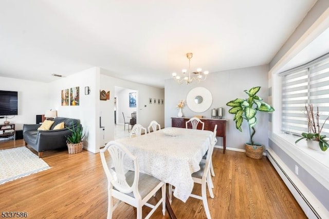 dining area featuring a notable chandelier, light hardwood / wood-style floors, and a baseboard heating unit