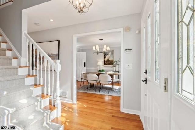 entryway with a chandelier, wood finished floors, visible vents, baseboards, and stairs