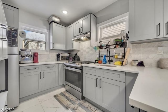 kitchen with gray cabinets, gas stove, sink, and tasteful backsplash