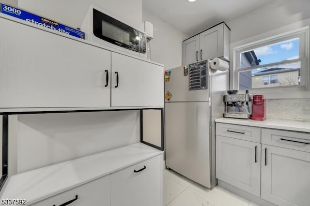 kitchen featuring tasteful backsplash, stainless steel refrigerator, and white cabinets