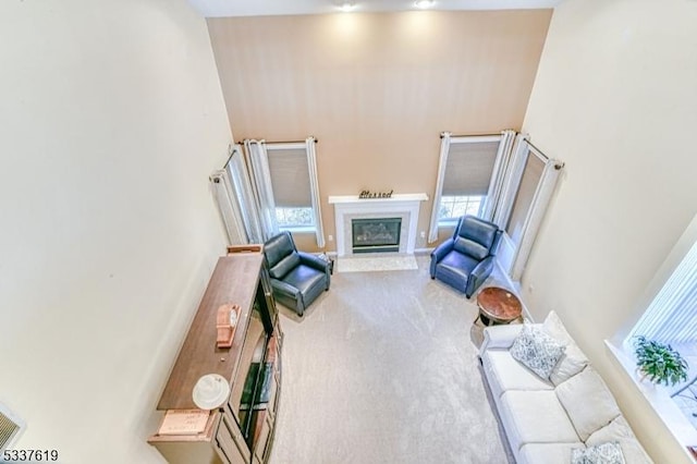 carpeted living area with a glass covered fireplace and a high ceiling