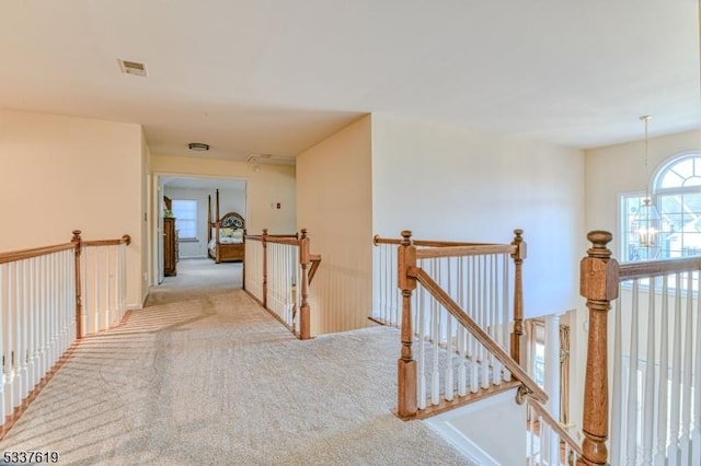 hall with visible vents, an upstairs landing, carpet, and a notable chandelier