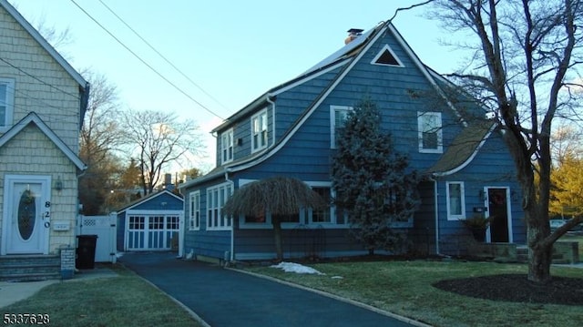 view of home's exterior with a lawn, driveway, a chimney, and an outdoor structure