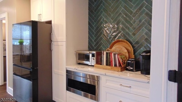 kitchen featuring built in microwave, white cabinetry, freestanding refrigerator, and light stone countertops