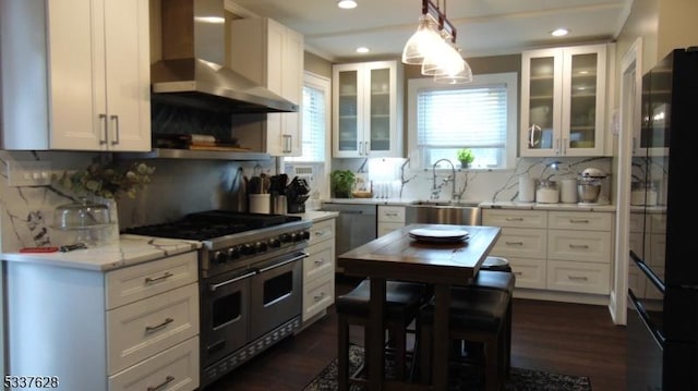 kitchen with light stone counters, white cabinets, stainless steel appliances, wall chimney exhaust hood, and a sink