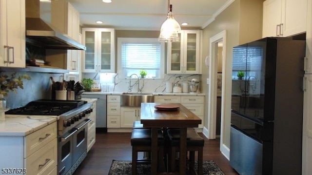 kitchen with range with two ovens, freestanding refrigerator, a sink, white cabinets, and wall chimney exhaust hood