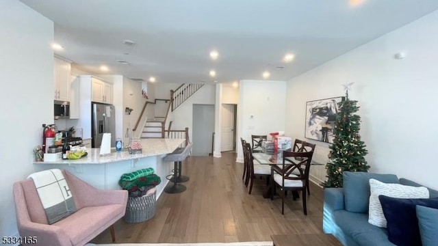 kitchen with appliances with stainless steel finishes, hardwood / wood-style floors, white cabinetry, a kitchen bar, and kitchen peninsula