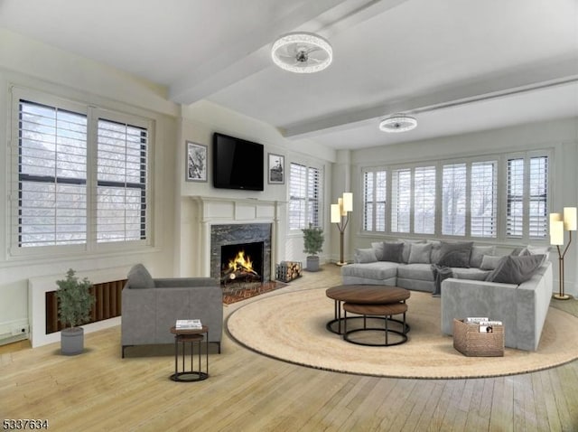 living room featuring beamed ceiling, a fireplace, and light wood-type flooring