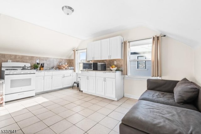 kitchen featuring lofted ceiling, light tile patterned floors, white range with gas stovetop, backsplash, and white cabinets