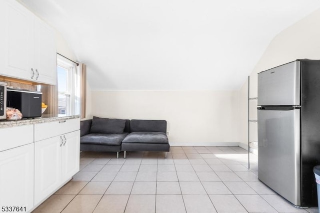 interior space with white cabinetry, vaulted ceiling, light tile patterned floors, and stainless steel fridge