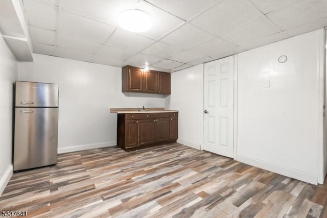 kitchen featuring sink, stainless steel refrigerator, dark brown cabinets, light hardwood / wood-style floors, and a drop ceiling