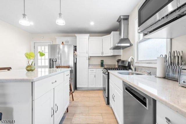 kitchen with pendant lighting, wall chimney range hood, white cabinetry, stainless steel appliances, and light stone counters