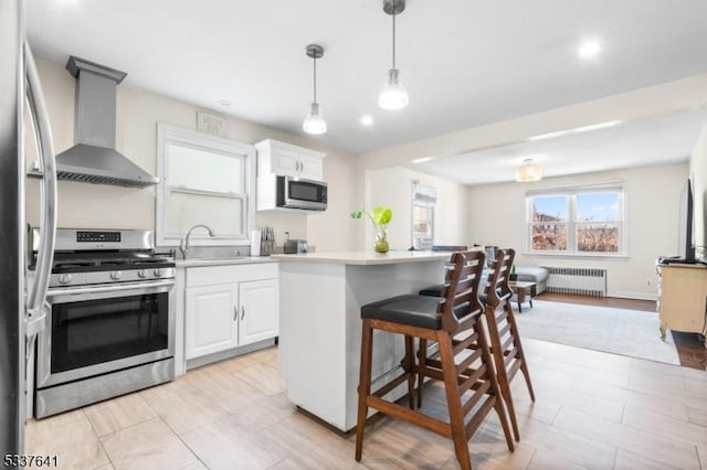 kitchen with white cabinetry, radiator, wall chimney exhaust hood, and appliances with stainless steel finishes