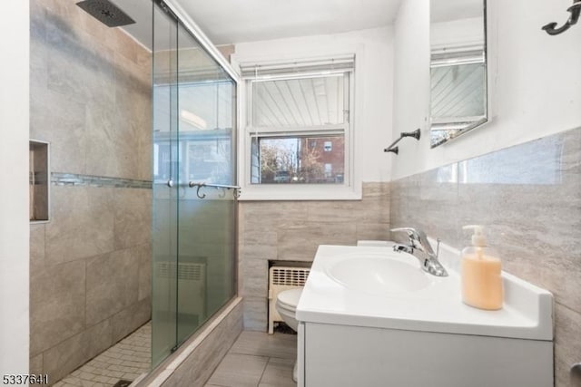 bathroom with radiator heating unit, tile walls, vanity, walk in shower, and toilet