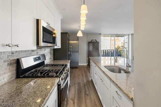 kitchen featuring stainless steel appliances, tasteful backsplash, hanging light fixtures, white cabinetry, and a sink