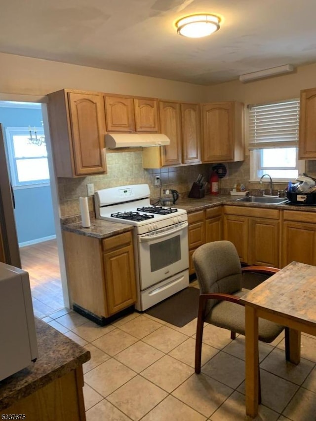 kitchen with sink, light tile patterned floors, light brown cabinets, white gas range oven, and decorative backsplash