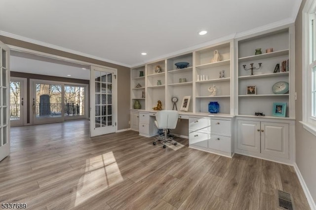 unfurnished office with built in desk, french doors, visible vents, and light wood-style flooring