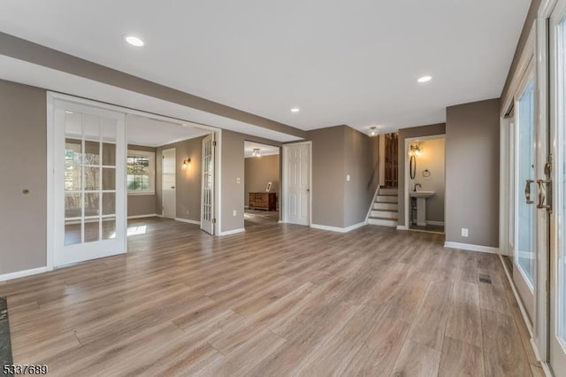 unfurnished living room with french doors, stairway, light wood-type flooring, and baseboards