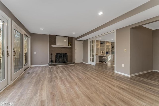 unfurnished living room featuring light wood-type flooring, french doors, a brick fireplace, and baseboards