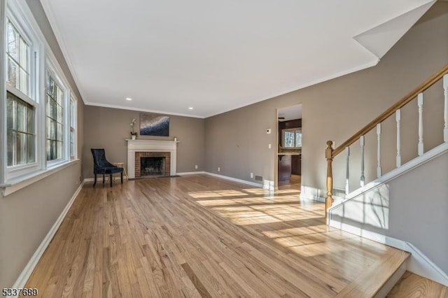 unfurnished living room featuring stairway, ornamental molding, a brick fireplace, wood finished floors, and baseboards