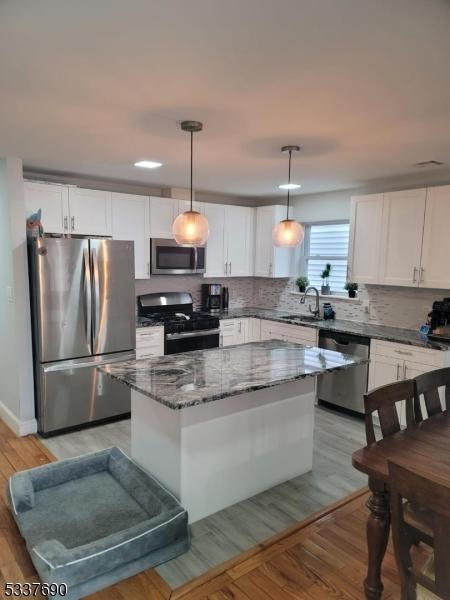 kitchen featuring decorative light fixtures, white cabinetry, sink, a center island, and stainless steel appliances