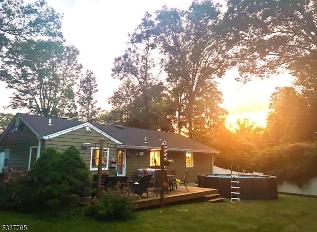 back house at dusk featuring a hot tub, a deck, and a lawn