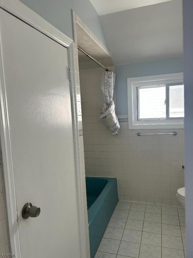 bathroom with lofted ceiling, tile patterned floors, toilet, and tile walls